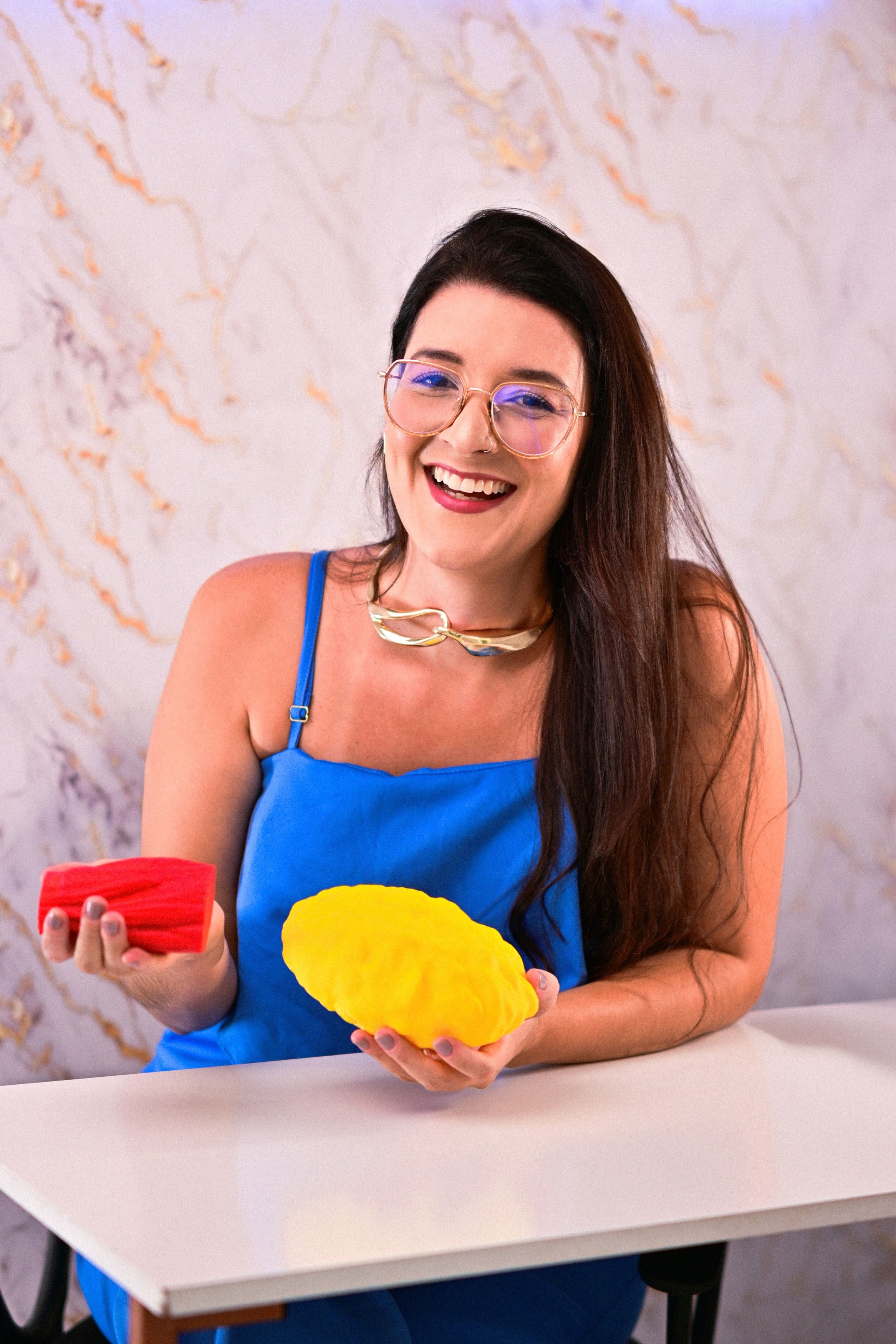 Nancy Drumond sorrindo, sentada, com modelos de alimentos nas mãos